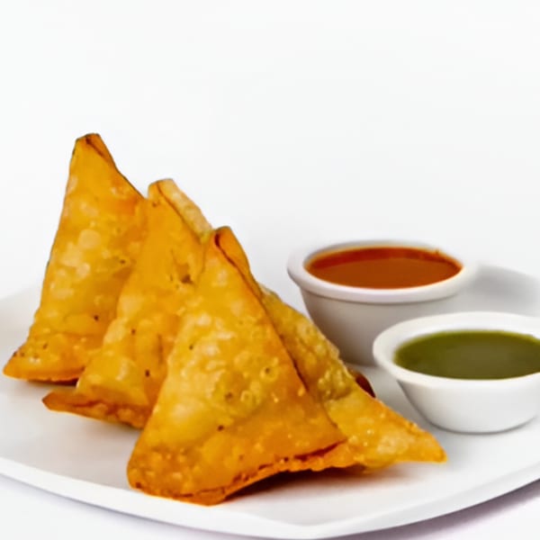 Three golden-fried samosas with two dipping sauces, red and green, on a white plate.