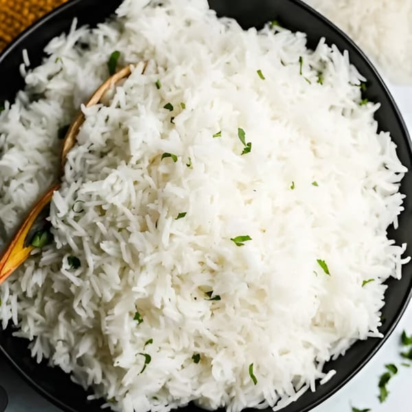 Fluffy white basmati rice, garnished with fresh green herbs, in a black bowl with a wooden spoon.