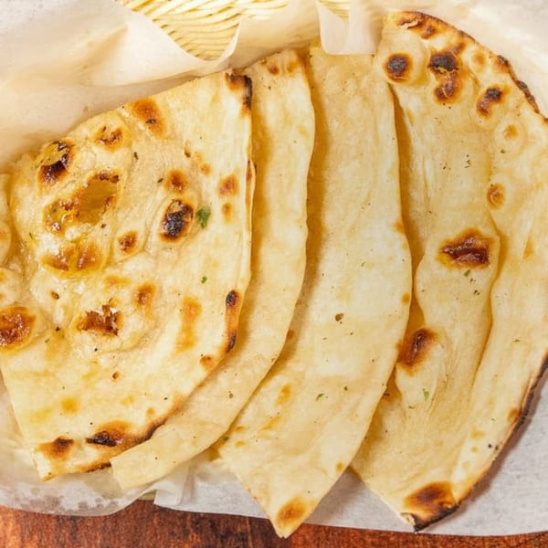 Golden-brown Indian naan bread, lightly charred, served in a basket lined with parchment paper.