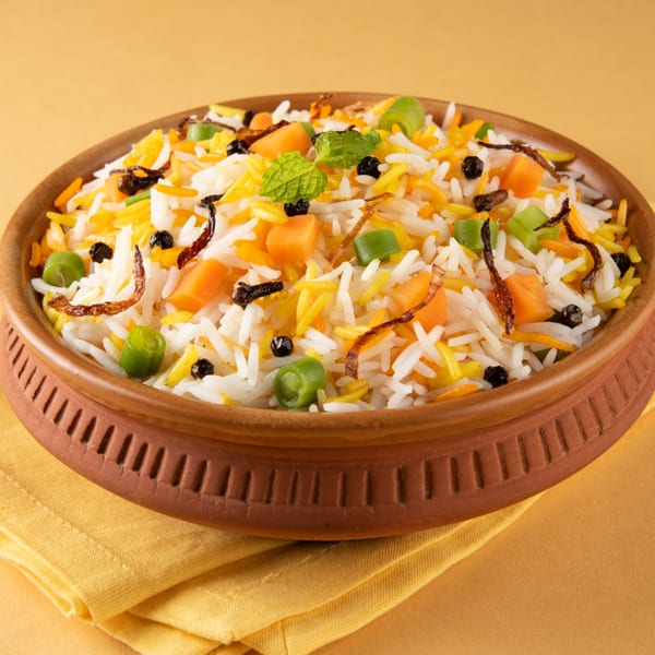Desi Flavors Indian Cuisine's vegetable biryani with rice, carrots, peas, and mint in a clay bowl.