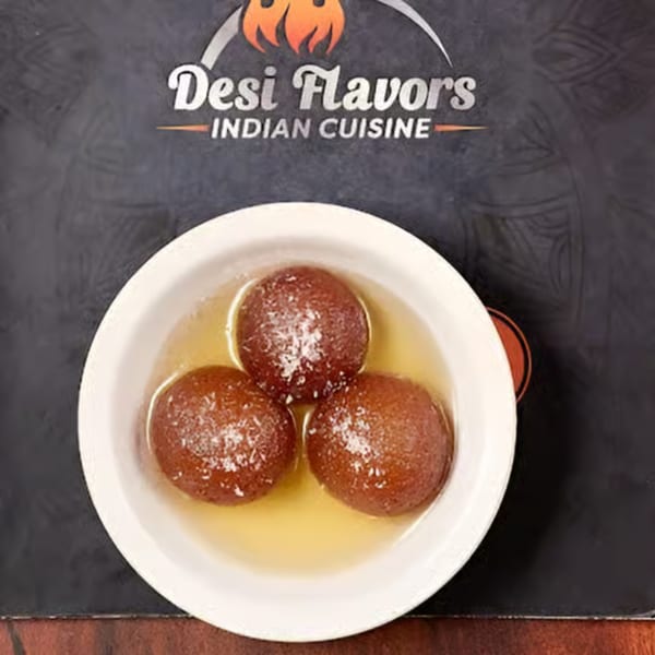 Three gulab jamun, Indian fried dough balls in syrup, sprinkled with coconut flakes in a white bowl.