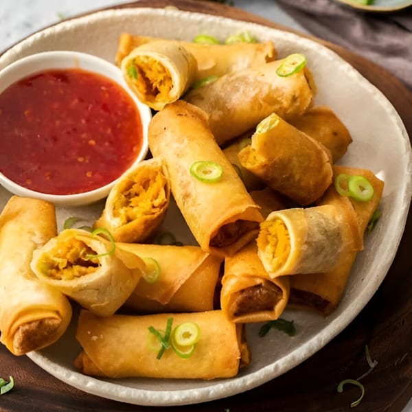 Crispy golden spring rolls with a savory filling, garnished with green onions, served with red dipping sauce.